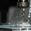 High-speed close-up of CNC drill bit in action with water splash for lubrication.