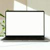 A sleek laptop with a white screen on a desk with green plants in the background.
