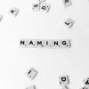 Flat lay of scattered Scrabble tiles spelling 'NAMING' on a white background.