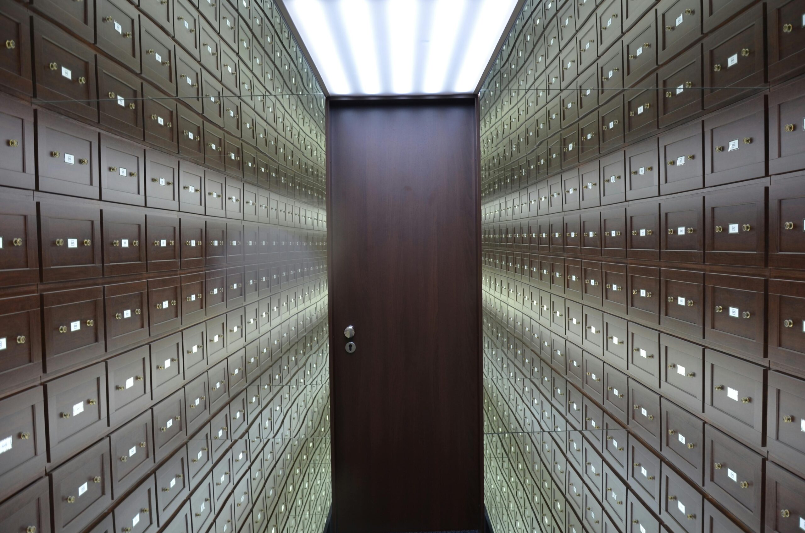 Wooden lockboxes line the walls of a modern, secure vault with a central wooden door.