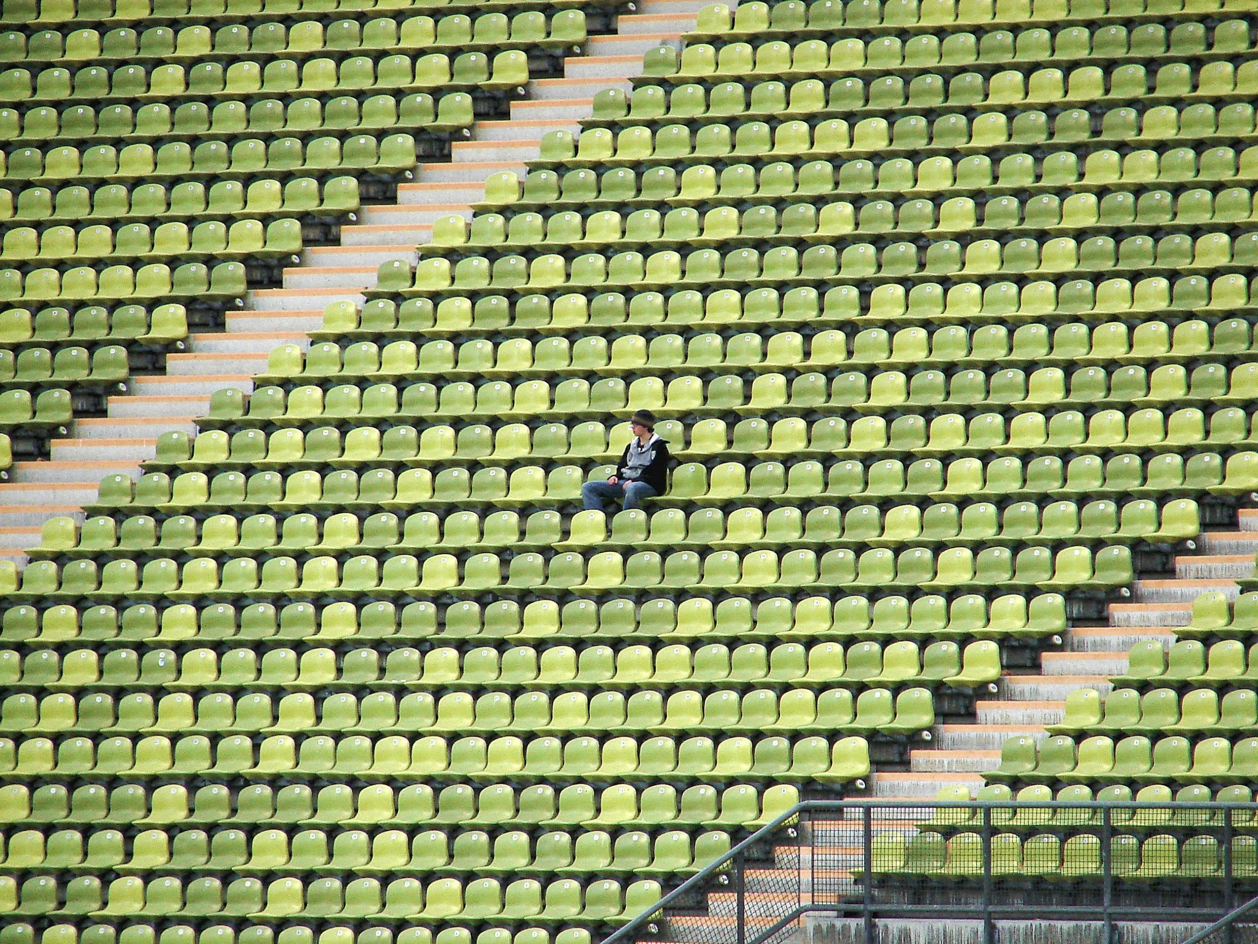 A solitary figure sits among green and yellow stadium seats, capturing a moment of solitude in München, Germany.